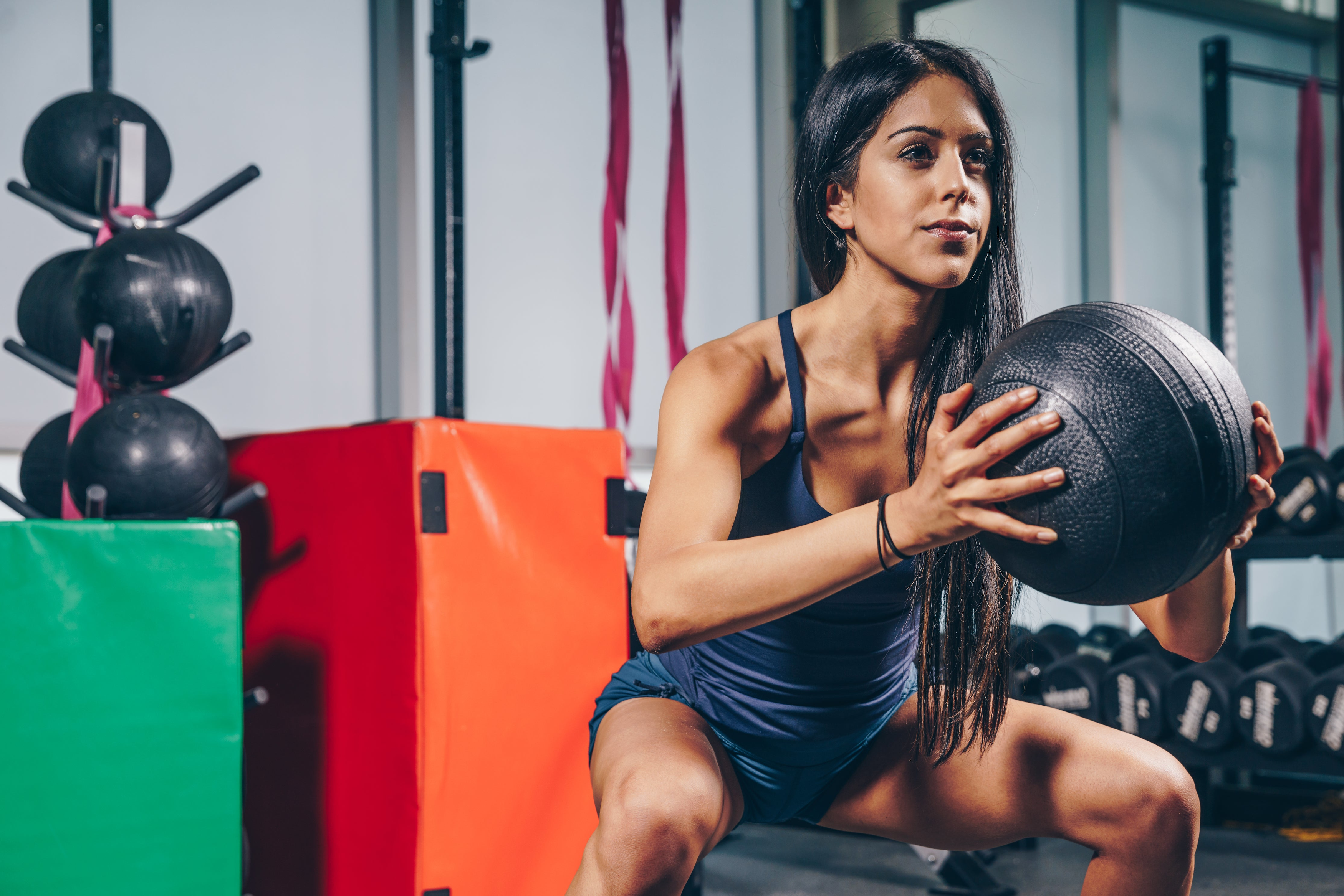 Woman in a squating possition in gym setting holding a weight ball in her hands